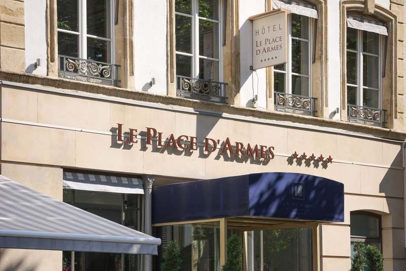 The stone facade of Le Place d'Armes, its name in bronze letters above the entrance.