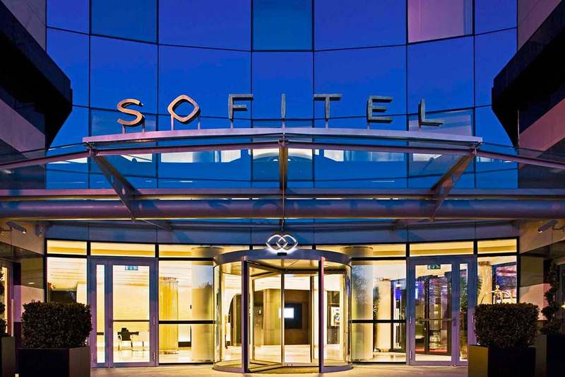 The lit glass entrance of the Sofitel Le Grand Ducal at dusk.